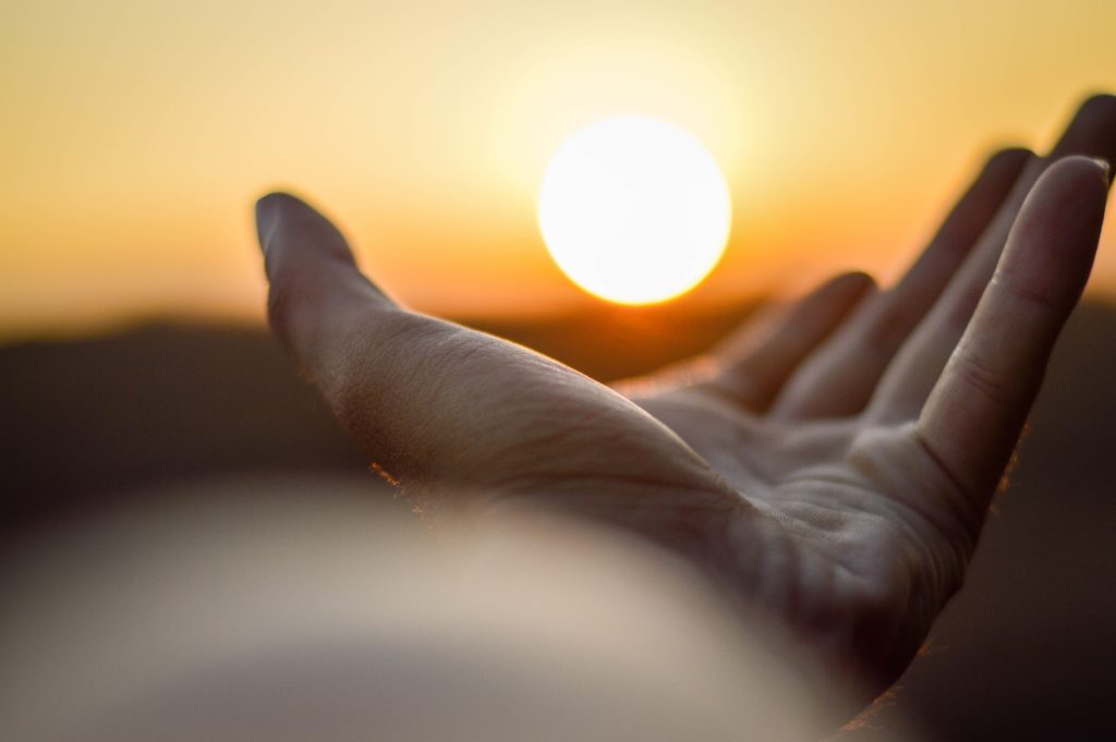 Image is of hand reaching to sun to demonstrate awakening to consciousness 