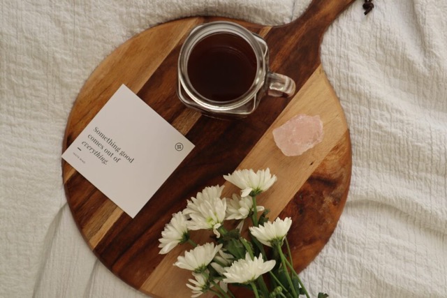 overhead flatlay shot of affirmation card with flowers, rose quartz crystal and tea 