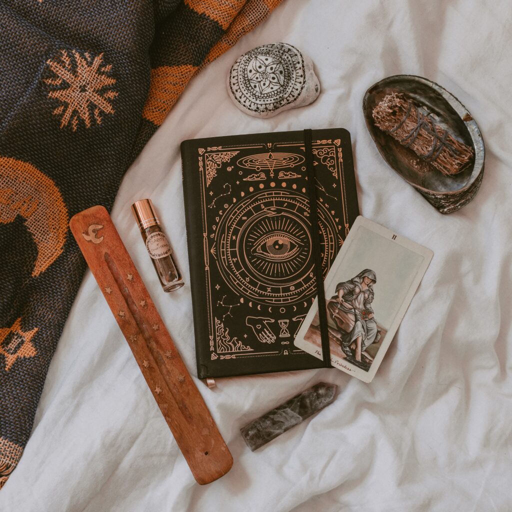 Journal surrounded by spiritual tools like Tarot cards, insense, crystals and sage
