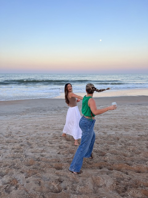 A manifesting generator dancing with a friend on the beach, celebrating her ability to change her mind 